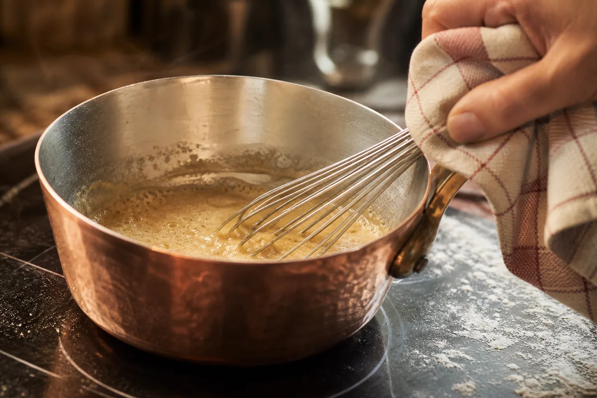 Roux blanc en train de blondir dans une casserole en cuivre, fouet en action